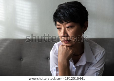 Close-up Senior Asian woman sitting on a couch at her home, an unhappy elder woman lost in thoughts missing remembering past, feeling lonely and solitude. Stock foto © 