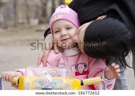 A little girl sat on the bike. Mom leaned over to her and kisses her. A warm spring day.