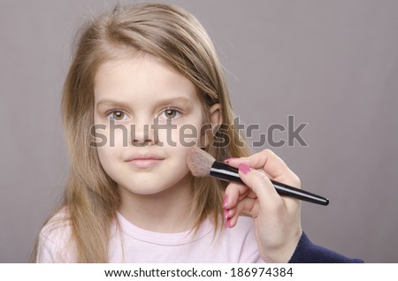 Makeup artist deals powder brush on the face of a five year old girl