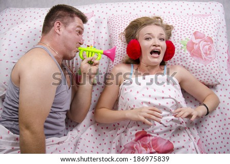 Young couple lying in bed. The guy woke girl blowing in tune. The girl in shock. Top view