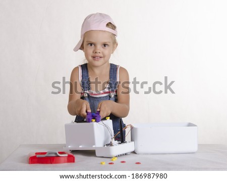 Girl playing in the repairer and repairs toy microwave. A girl Holds the pliers and twisted them nut and looks in a frame