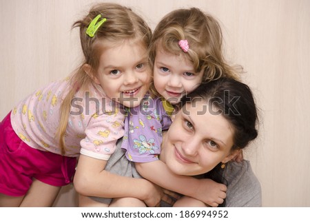 family of the house, my mother, two-year and four-year-old daughter. The younger daughter hung on the mother\'s neck, the eldest daughter lay down on shoulder of the younger. Smile and look in frame.