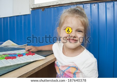 Girl sitting on the veranda at the table and playing a Board game with a mosaic with letters on it. The girl put this in the right eye with the letter of the mosaic