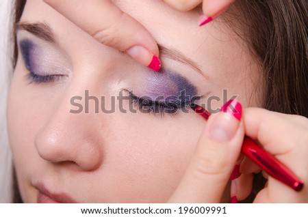 Makeup artist draws arrows beautiful young girl in the makeup