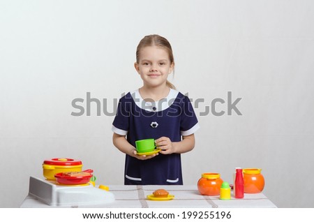 Five year old girl plays children\'s dishes at a table covered with a cloth