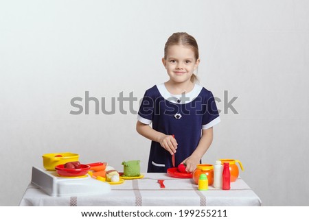 Five year old girl playing in a children's mistress dishes at a table covered with a cloth