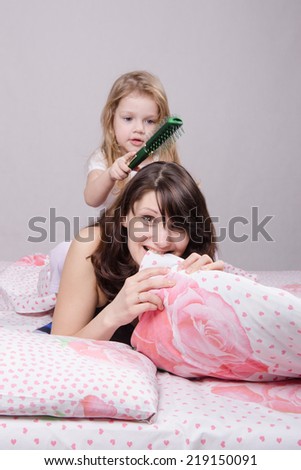 Daughter mother combing her hair lying in bed