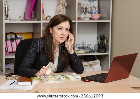 Amazed girl holding a wad of money and talking on phone in office