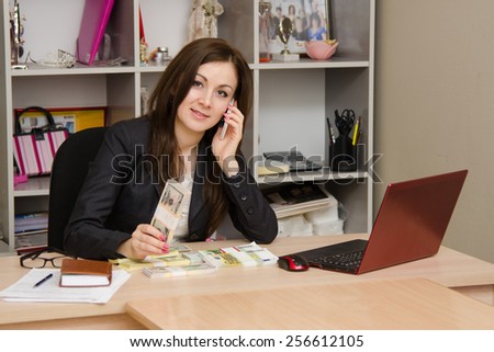 Business woman at a desk with stack of money talking on phone