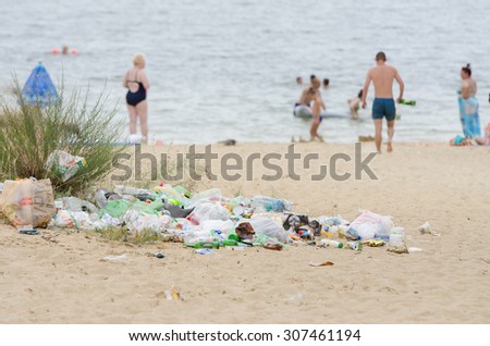 Volgograd, Russia - July 3, 2015: A pile of garbage in the sand on the bank of the river in the background people bathe in the river
