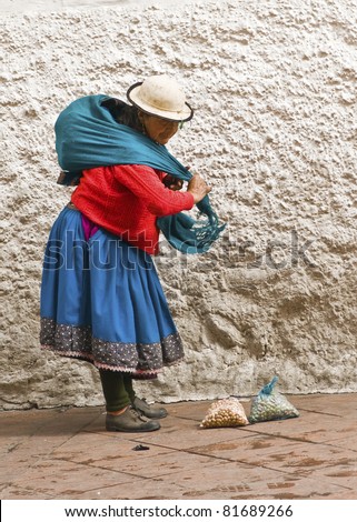 CUENCA, ECUADOR - MAY 27: Indigenous woman packs up her fruits after selling on a market street on May 27, 2011 in Cuenca, Ecuador.She sells mostly hand crafted items, flowers and fruits.