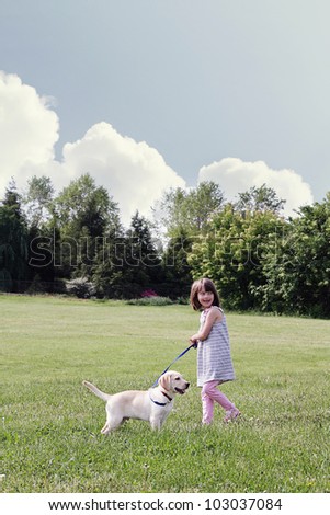 A happy little girl walks her puppy, an English Cream Labrador Retriever - Golden Retriever mixed designer breed, on a beautiful spring day. Extreme shallow depth of field.