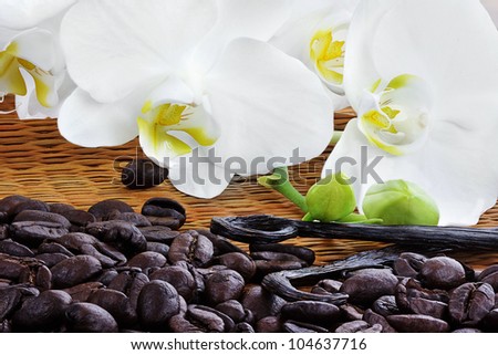 Beautiful white orchid blossoms with whole vanilla pods and rich roasted coffee beans on a bamboo mat.