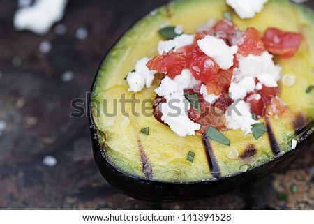 Grilled avocados filled with diced tomatoes and feta cheese and garnished with olive oil and freshly chopped parsley. Extremely shallow depth of field with selective focus on the foreground.