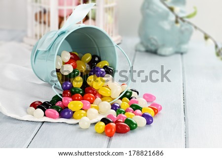 A blue tin bucket tipped over, spilling jelly beans onto a table. Shallow depth of field.