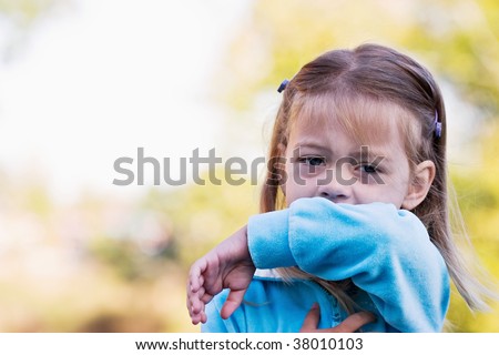 Little girl demonstrates coughing or sneezing into her elbow to avoid spreading unwanted germs.