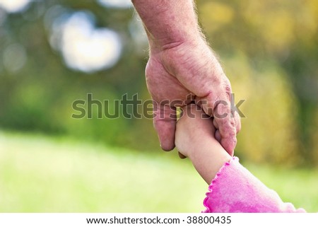 Father holding daughter\'s hand with bokeh in background in the shape of a heart. Could also be used as grandfather\'s hand.