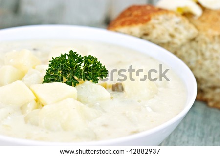 A bowl of freshly made creamy potato soup garnished with parsley. Extreme shallow DOF with focus on center of soup. Bread with butter in background.