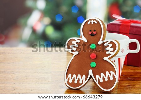 Gingerbread man cookie has been set out for Santa with a cup of milk. Christmas tree in the background. Selective focus on the gingerbread cookie.