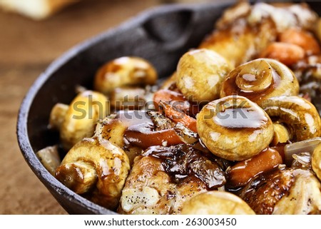 Detailed shot of Coq Au Vin in rustic cast iron pan with shallow depth of field.