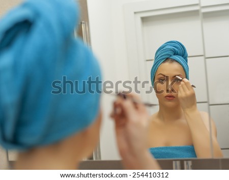 Young woman looking in the mirror and putting make-up on