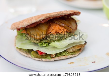 Delicious vegan burger with pea patty, grilled pear, grilled red preppers, shredded carrrot, iceberg salad, ketchup, pickles and onions on white plate