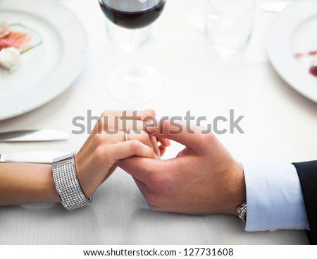 Closeup of a man holding his girlfriend\'s hand at the restaurant