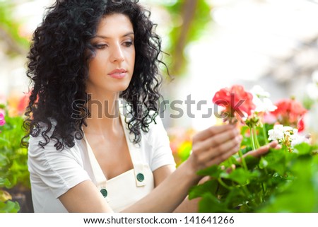 Beautiful female florist touching some flowers in a greenhouse