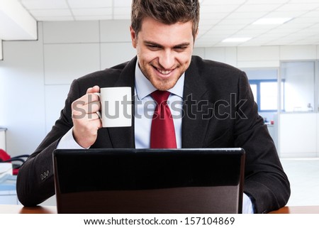 Happy businessman using a computer while drinking coffee