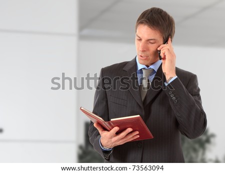 Businessman talking on a mobile phone while reading his agenda in an office environment