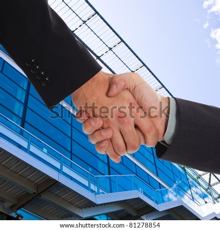 Handshake between businessmen. Hi-tech blue building and sky in the background.