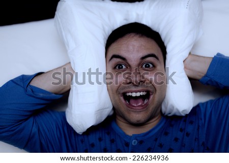 Insomniac man using a pillow to cover his ears