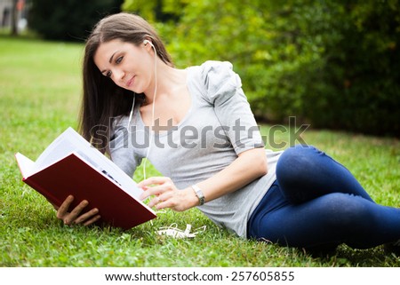 Woman reading a book while listening music in a park