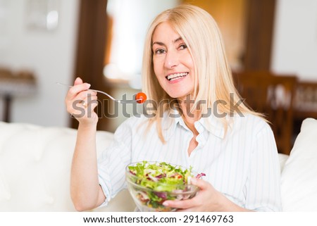 Portrait of a smiling woman eating an healthy salad in her living room
