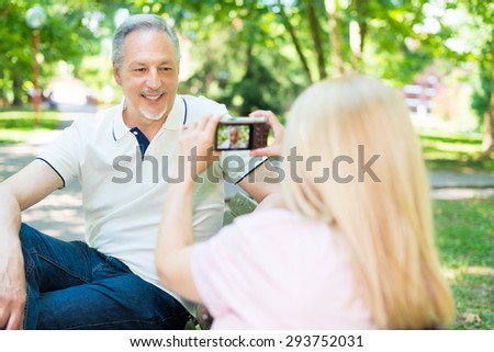 Wife using a compact camera to take a portrait of her husband in a park