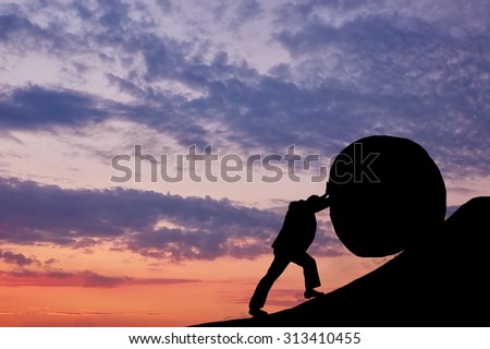 Business concept. The man is pushing the stone up the mountain at sunset