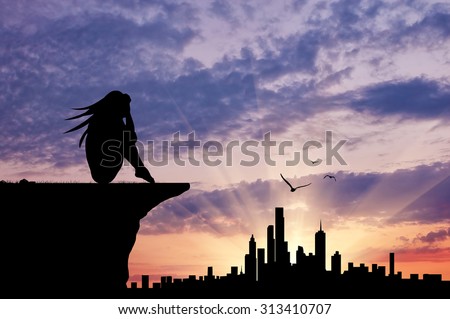 Concept of emotion. Silhouette of a sad woman sitting looking over the city at sunset
