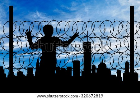 Safety concept. Silhouette of a refugee near the fence of barbed wire on the background of the city away