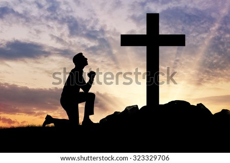 concept of religion. Silhouette of a man praying before a cross at sunset