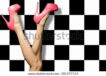 Female legs wearing summer high heels over black and white checkered background