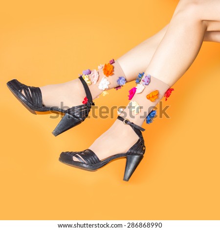 Female legs wearing summer clogs and funny floral socks over orange background