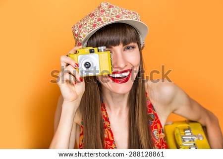 Happy hipster girl making photo with retro camera over orange background. camera painted in yellow by me, focus on face