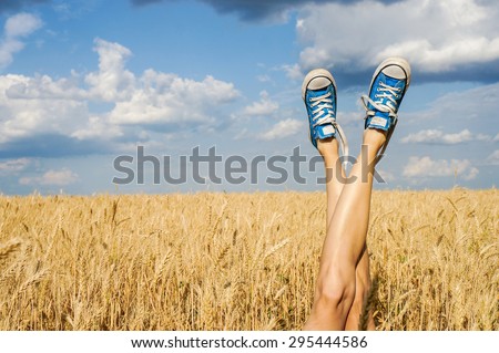 Sexy woman legs on blue sky and wheat  field background. Summer vacation concept