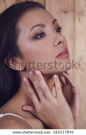 Portrait of young pretty tan woman touching her face.