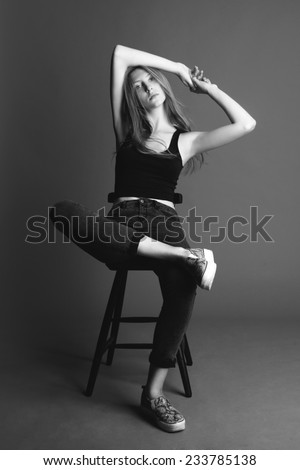 Young beauty blond woman seating on the chair, black and white, grey background.