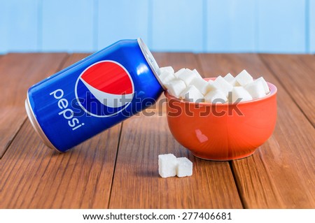 KIEV, UKRAINE - MAY 8, 2015: From can of Pepsi flowing sugar and fills a red bowl on wooden background. Pepsi is a carbonated soft drink that is produced and manufactured by PepsiCo.