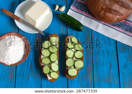 Freshly baked bread, sandwich with sliced cucumbers and butter on dish in rural or rustic kitchen at vintage wood table from above. Background