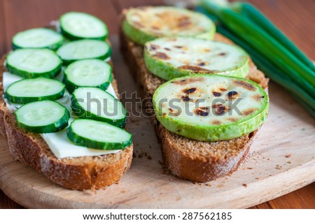 Open sandwich with butter, cucumber grilled vegetable marrow and green onion in rural or rustic kitchen at vintage wood table from above. Selective focus