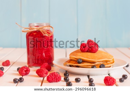 Stack of wheat golden pancakes or pancake cake with freshly picked blueberry on a dessert plate, glass mason jar full off raspberry jam