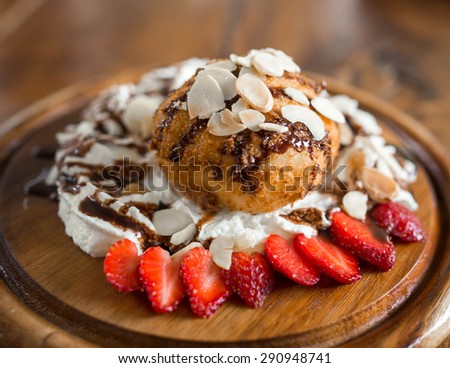 Fried ice cream with almond, whipped cream and strawberry on wood dish